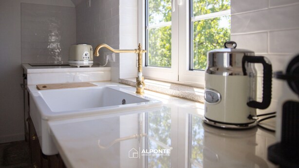 A modern kitchen with a white sink, a brass faucet, and a coffee maker on the counter. - Quinta da Costeira - Casa Azul do Limoal (Arcos de Valdevez)