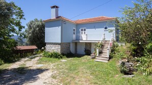 A two-story house with a red-tiled roof, a stone foundation, and a small garden with a staircase leading to the upper floor. - Quinta da Costeira - Casa Azul do Limoal (Arcos de Valdevez)
