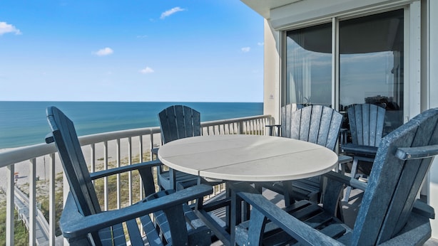 A balcony with a round table and four Adirondack chairs, overlooking a beach and ocean. - Spanish Key 605 | Oceanfront Condo | Steps from Flora Bama | My Beach Getaways (Pensacola)