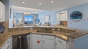 A kitchen with granite countertops, white cabinetry, a stainless steel dishwasher, and a large clock on the wall. - Spanish Key 605 | Oceanfront Condo | Steps from Flora Bama | My Beach Getaways (Pensacola)
