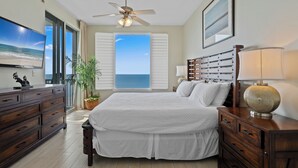 A bedroom with a bed, a ceiling fan, a TV, a dresser, a lamp, and a view of the ocean. - Spanish Key 605 | Oceanfront Condo | Steps from Flora Bama | My Beach Getaways (Pensacola)