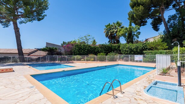 Una piscina rectangular con un borde de baldosas de piedra, rodeada por una valla metálica y árboles.