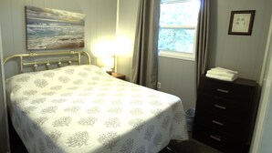 Ett sovrum med en säng, ett nattduksbord, en byrå, ett fönster med gardiner och en tavla på väggen.