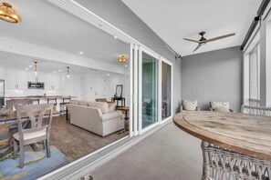 A modern living room with a sofa, dining table, and chairs. There is a kitchen area with white cabinets and a microwave.