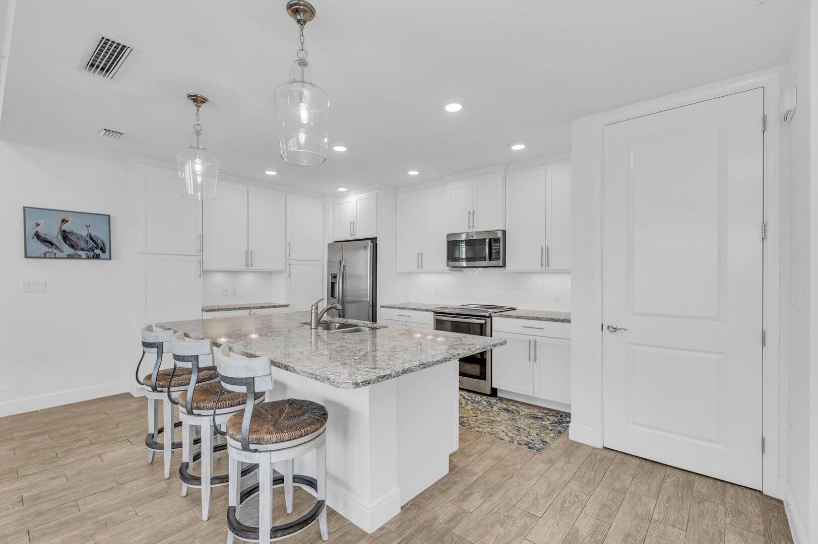 A modern kitchen with white cabinets, a central island with bar stools, stainless steel appliances, and pendant lighting.