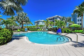 A pool area with a clear blue pool, lounge chairs, and palm trees.