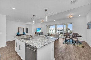 A modern kitchen with a large island, a dining area with a view, and a balcony with a table and chairs. - One Particular Harbour Penthouse - Anna Maria Island - Beach (Bradenton)