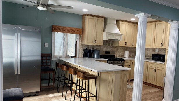 A modern kitchen with a central island, bar stools, a refrigerator, and wooden cabinets.