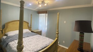 A four-poster bed with a wooden headboard, a bedside table with a lamp, and a window with curtains.