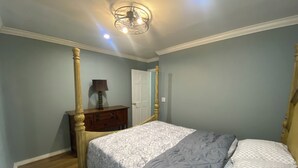 A bedroom with a bed, wooden headboard, a dresser, a lamp, and a door.