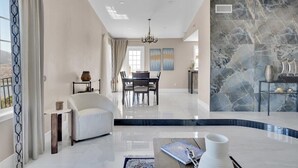 A spacious living area with a dining table, a sofa, and a marble accent wall. - Luxury 4 BR w/ Serene Lake Views (Spring Valley)