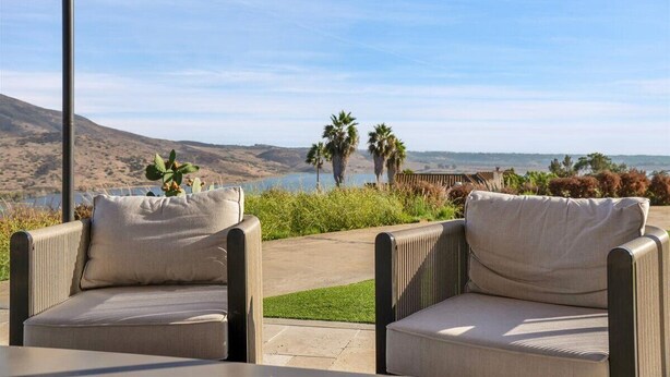 An outdoor seating area with two cushioned chairs and a table, overlooking a scenic landscape with hills and a body of water. - Luxury 4 BR w/ Serene Lake Views (Spring Valley)