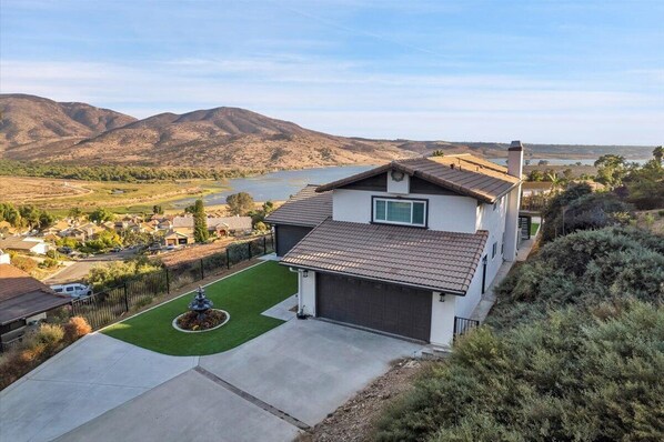 A two-story house with a garage, a well-maintained lawn, and a view of a lake and mountains in the background.