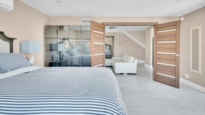 A modern bedroom with a large bed, a glass wardrobe, a white sofa, and a wooden door. - Luxury 4 BR w/ Serene Lake Views (Spring Valley)