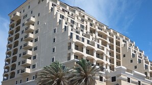 A multi-story hotel with balconies, palm trees, and a clear blue sky.
