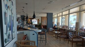 A spacious cafe with wooden flooring, modern pendant lighting, and large windows offering views of the street.