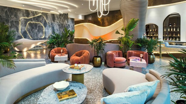 A modern lobby with curved seating, a central light fixture, and a bar area with shelves. - UNFRAMED, Autograph Collection (Miami Beach)