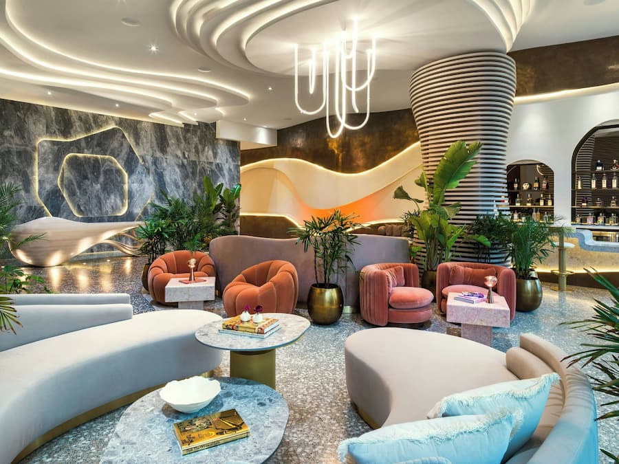 Um lobby moderno com assentos curvos, um lustre central e um espaço bar com prateleiras.