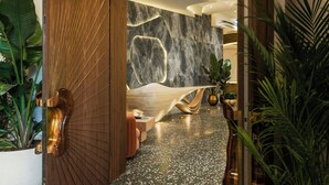 A modern lobby with a marble wall, wooden door, and potted plants. - UNFRAMED, Autograph Collection (Miami Beach)