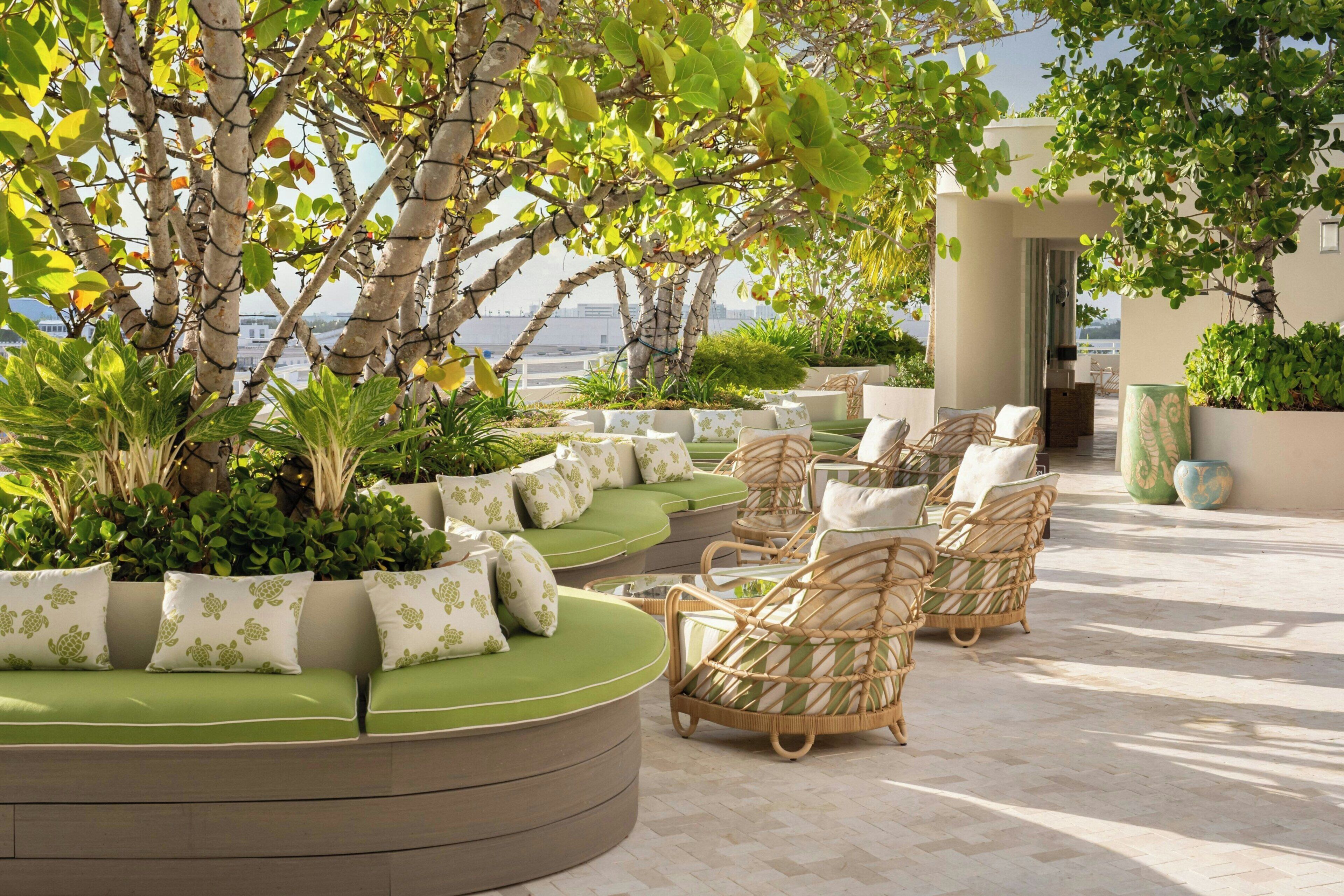 Une terrasse sur le toit, dotée de sièges confortables avec des coussins verts, de chaises en osier et de plantes en pot.