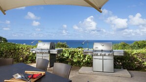 Un patio al aire libre con dos parrillas de barbacoa, una mesa con utensilios y vista al océano.