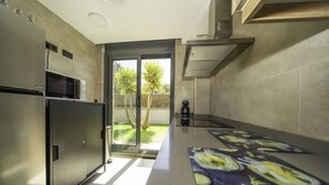 Eine moderne Küche mit einem Edelstahl-Kühlschrank, einer Mikrowelle und einem Einbauofen. Eine Glastür führt auf eine Terrasse mit Blick auf Palmen.