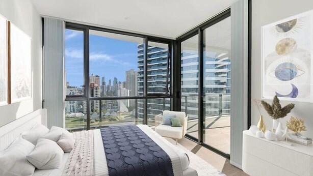 Une chambre moderne avec un grand lit, une commode blanche et une vue sur la ville grâce à de grandes fenêtres du sol au plafond.