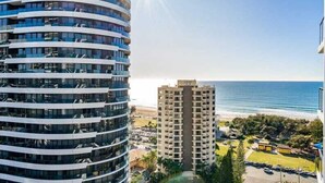 Un immeuble de grande hauteur à la façade incurvée, offrant une vue sur la plage et disposant d’un espace de stationnement en premier plan.