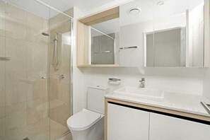 Un baño moderno con ducha de vidrio, inodoro blanco y tocador con espejo.
