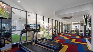 Une salle de sport équipée de tapis de course, d’appareils d’exercice et de grandes fenêtres offrant une vue sur la ville.
