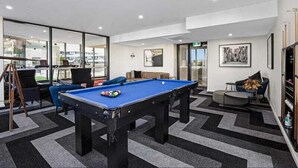 Un espace piscine intérieur moderne, doté d’une table de billard, de sièges confortables et de grandes fenêtres offrant une vue panoramique.