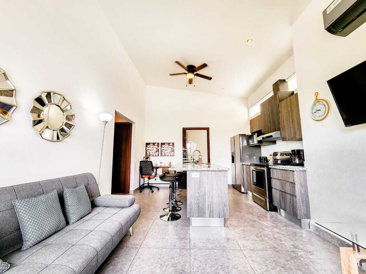 A modern kitchen with a central island, a grey sofa, and a ceiling fan.
