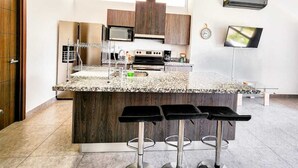 Een moderne keuken met een granieten aanrechtblad, roestvrijstalen apparatuur en een inbouwwijnbar met barkrukken.