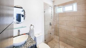 Een moderne badkamer met een douchecabine van glas, een witte wastafel en een toilet.