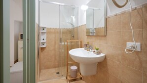 Un baño con ducha envuelta en vidrio, un lavabo con espejo y un perchero para toallas.