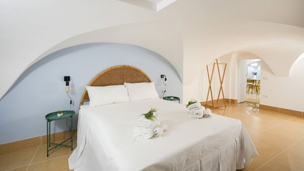 Un dormitorio con una cama, dos mesitas de noche y una mesa auxiliar verde, además de un techo abovedado grande.