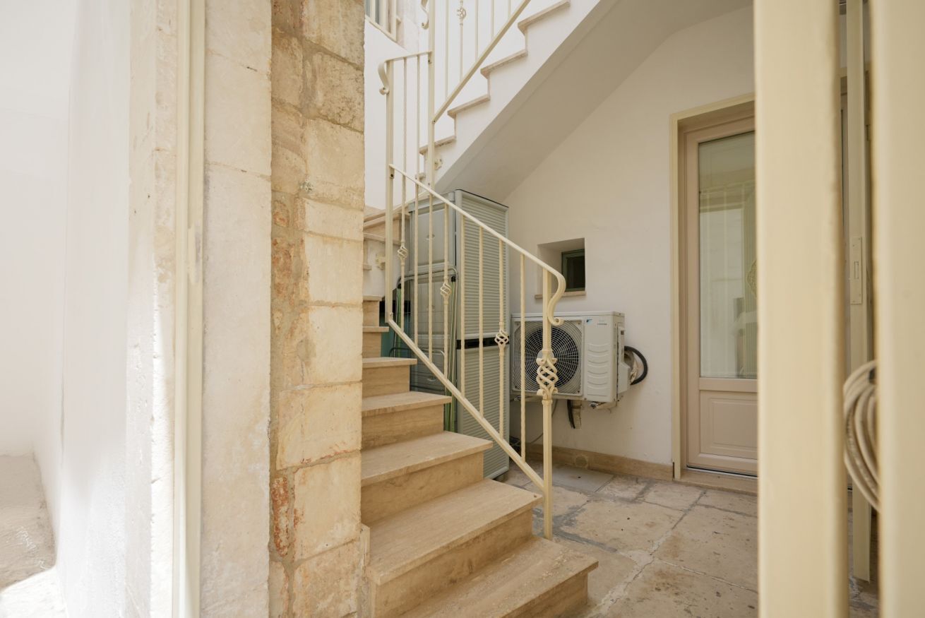 Una escalera con barandilla blanca, un muro de piedra y una unidad de aire acondicionado en la pared.