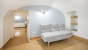 Una habitación con sofá, cama y una pequeña estantería con vasos.