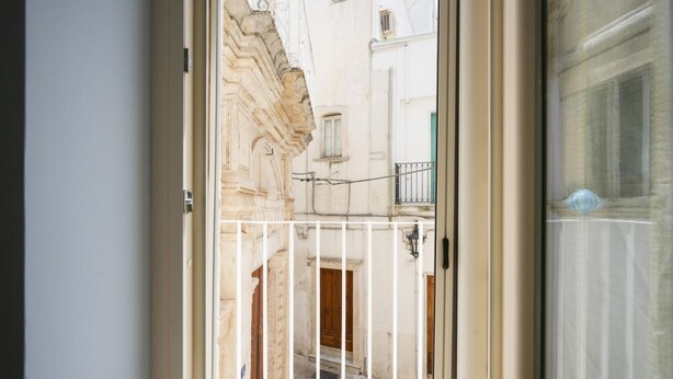 An open door to a narrow courtyard with a stone wall, a wooden door, and a metal gate.