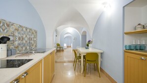 A kitchen with a patterned backsplash, a dining area with chairs, and a hallway leading to another room.