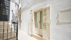 A narrow corridor with a white wall, a wooden door with a glass panel, and a metal railing.