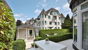 Ein Wohngebiet mit einem weißen Haus, einem kleinen Gartenhaus und einem ordentlich geschnittenen Heckenstreifen.