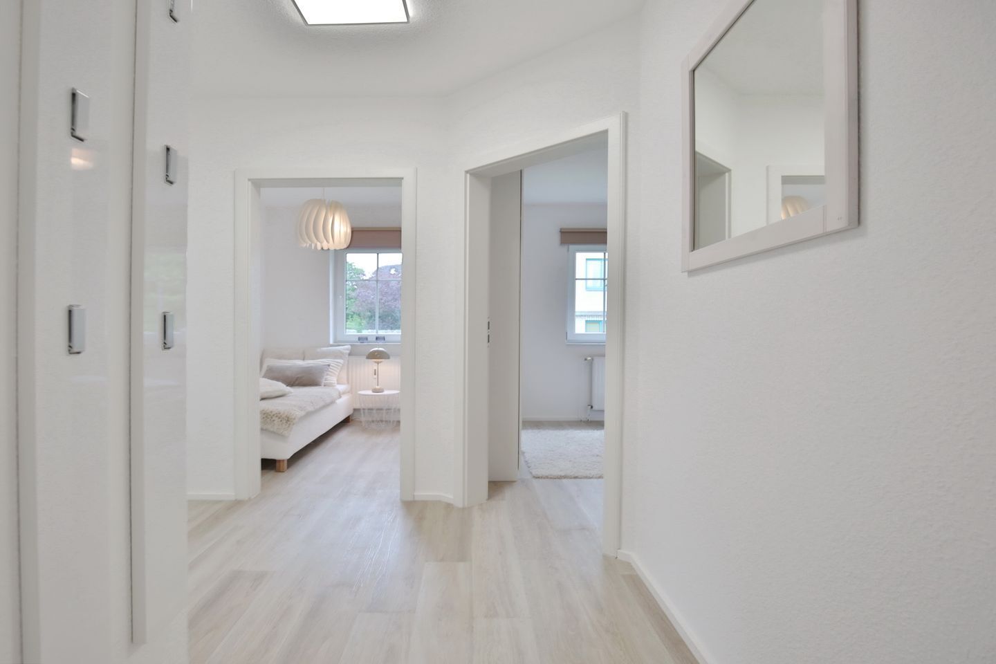 Un pasillo moderno y bien iluminado con diseño minimalista, que conduce a un dormitorio con cama y una lámpara colgante.