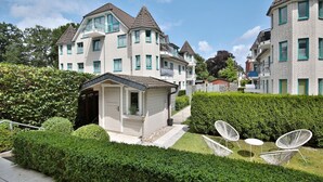 Ein Wohngebiet mit mehreren zweistöckigen Häusern, einer kleinen Gartenhütte und einem gepflegten Garten mit weißen Stühlen.