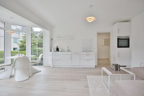Une cuisine moderne avec des meubles blancs, un four encastré et un coin repas comprenant une table et des chaises blanches.