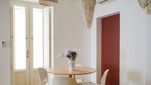 Een eethoek met een ronde tafel, witte stoelen, een vaas met bloemen en een rode accentmuur.