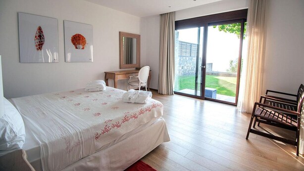 Un dormitorio con cama, escritorio, silla y vista a un jardín por una puerta corredera.