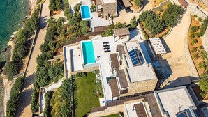 Vista aérea de una propiedad costera con varias construcciones, una piscina y vegetación circundante.