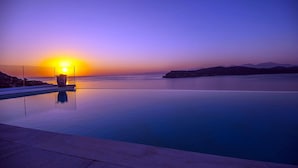 Una tranquila piscina infinita con vista al atardecer, cielo despejado y montañas a lo lejos.