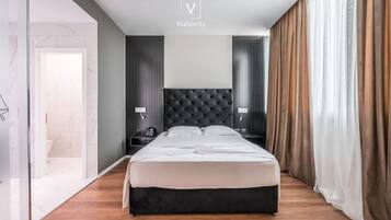 A modern hotel room with a large bed, a dark tufted headboard, bedside tables with lamps, and a view of a bathroom.